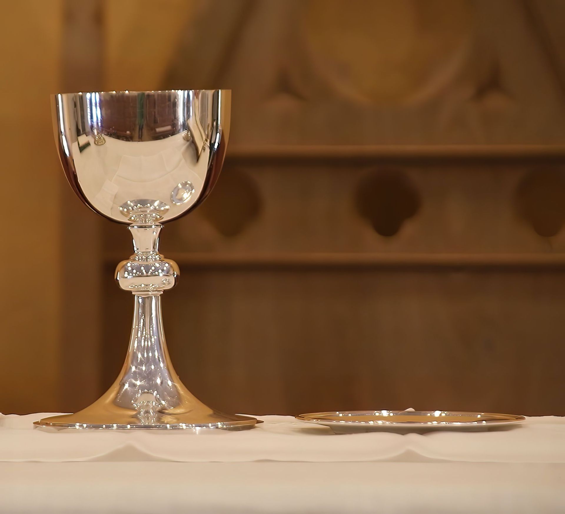 A clear goblet and a small plate on a white tablecloth against a warm brown background.