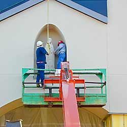 Two workers on a lift removing a statue from an arched alcove in a building.