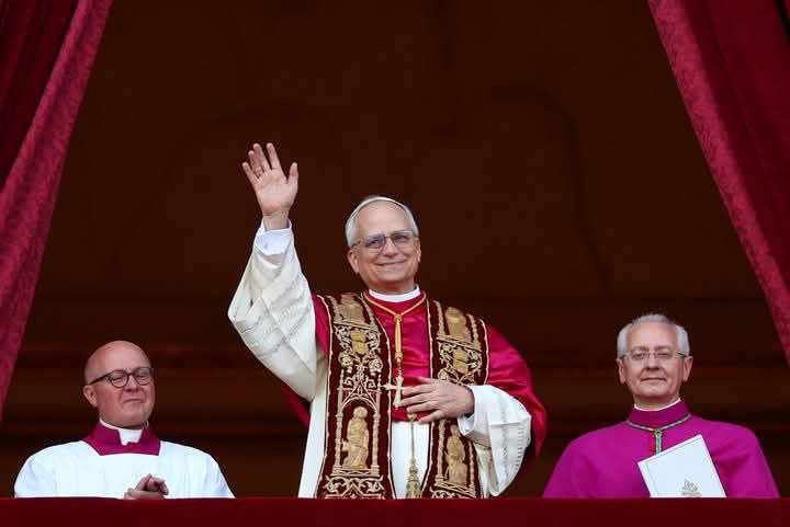 Pope in a red robe is waving from a balcony.