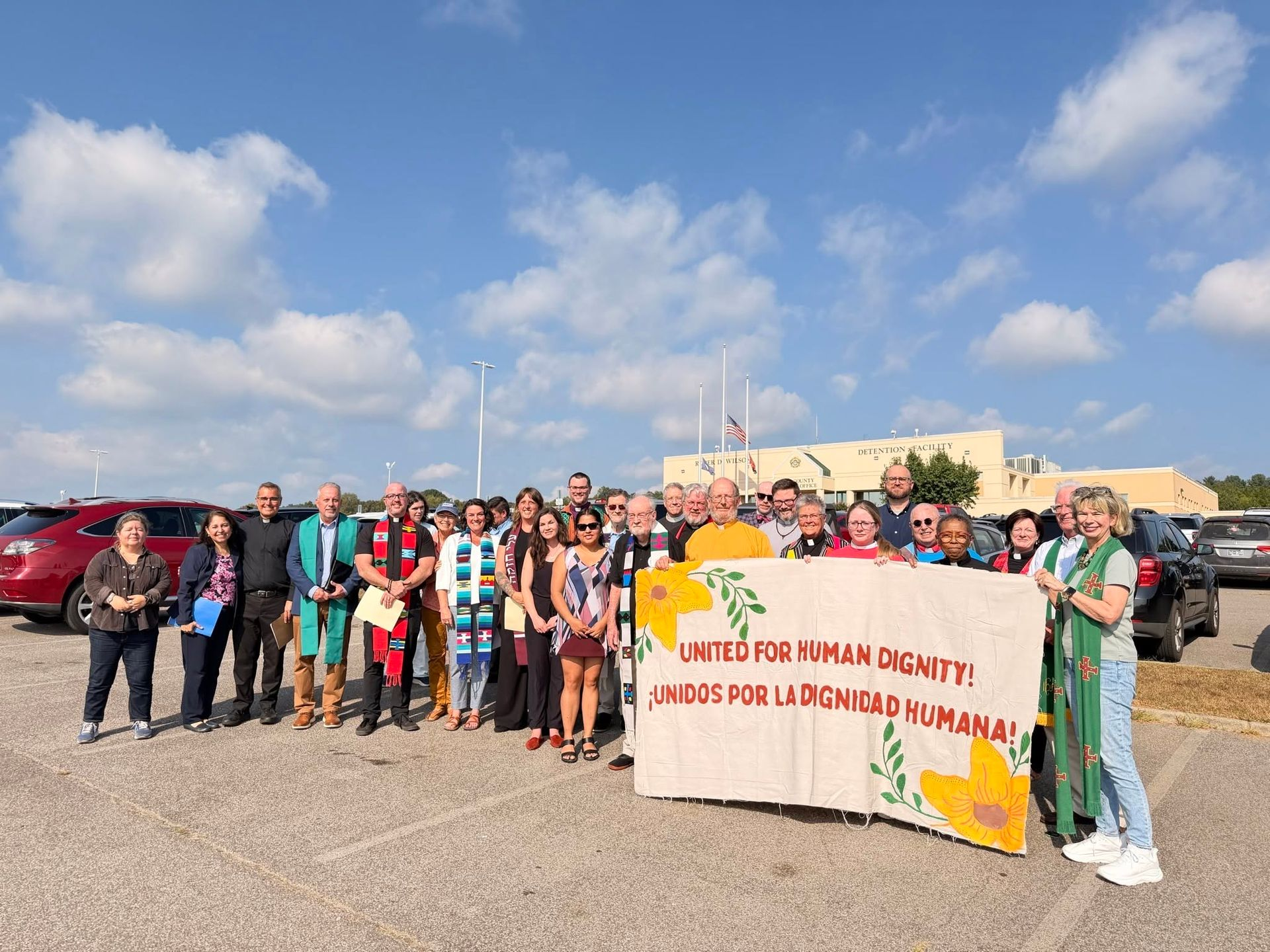 Group of people holding a banner in a parking lot under a partly cloudy sky