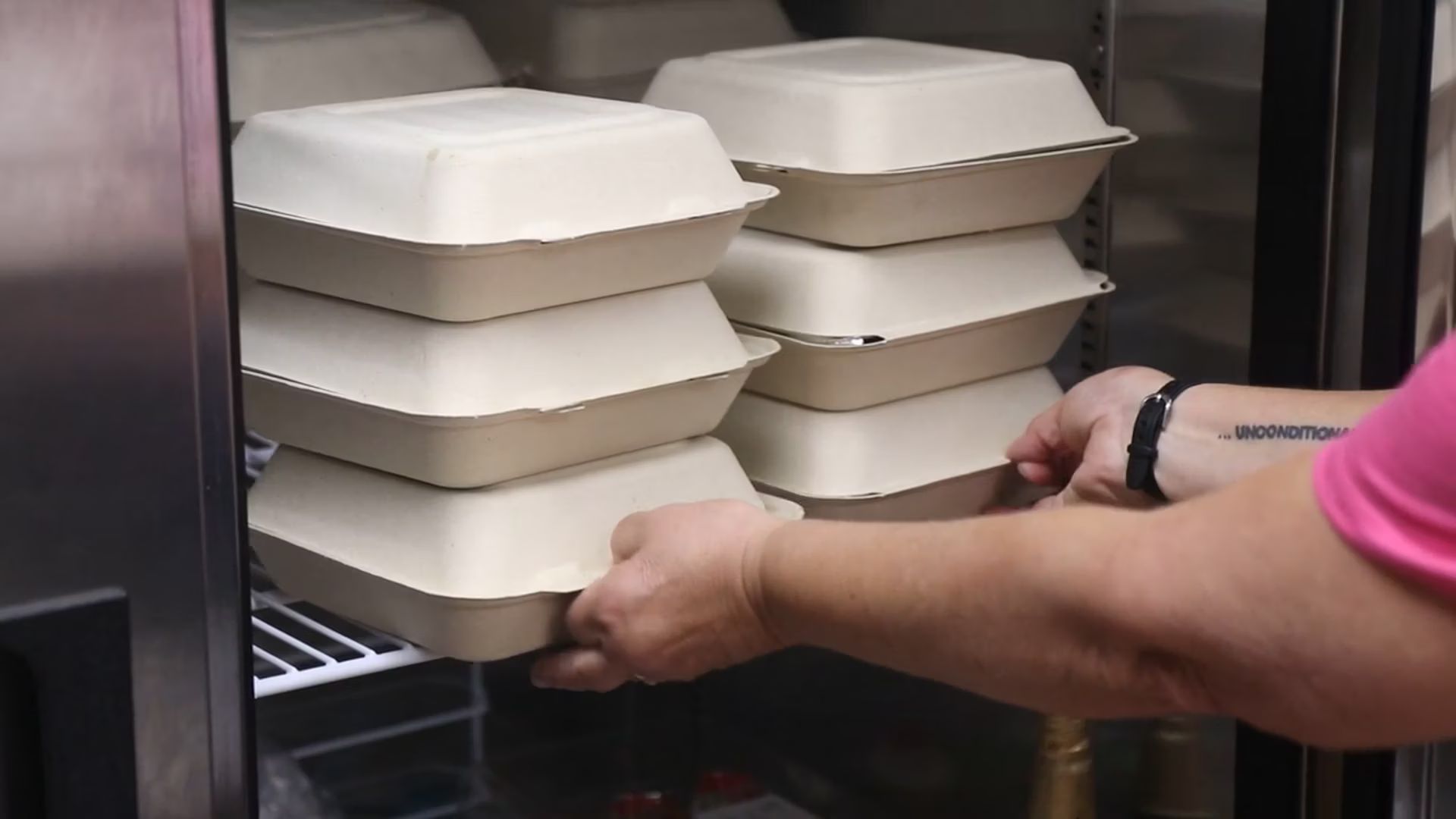 Person sliding stacked takeout containers onto a kitchen shelf.