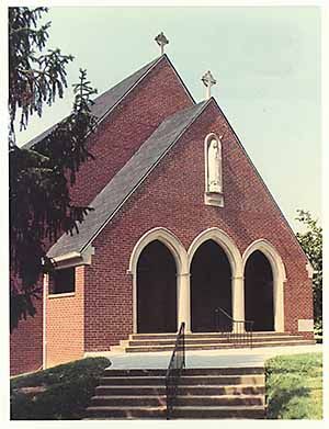Brick church with three arched doorways, steps, and a statue of Mary.