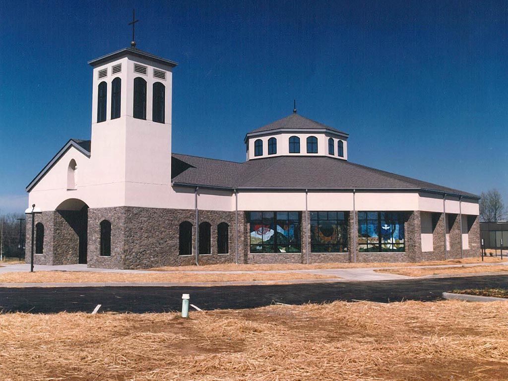 Church with tower and dome, beige walls, stone base, stained glass windows under a blue sky.