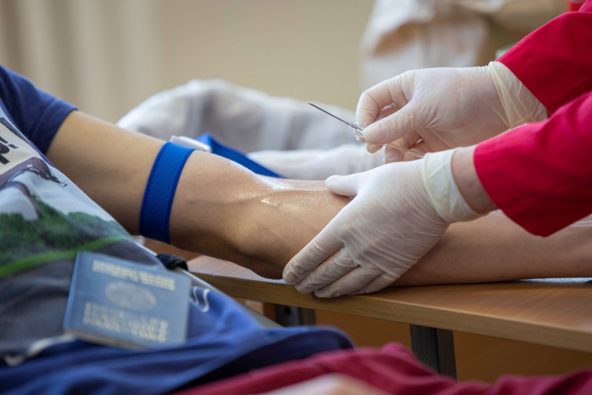Gloved medical worker drawing blood from a patient’s arm at a clinic, with a blue tourniquet attached