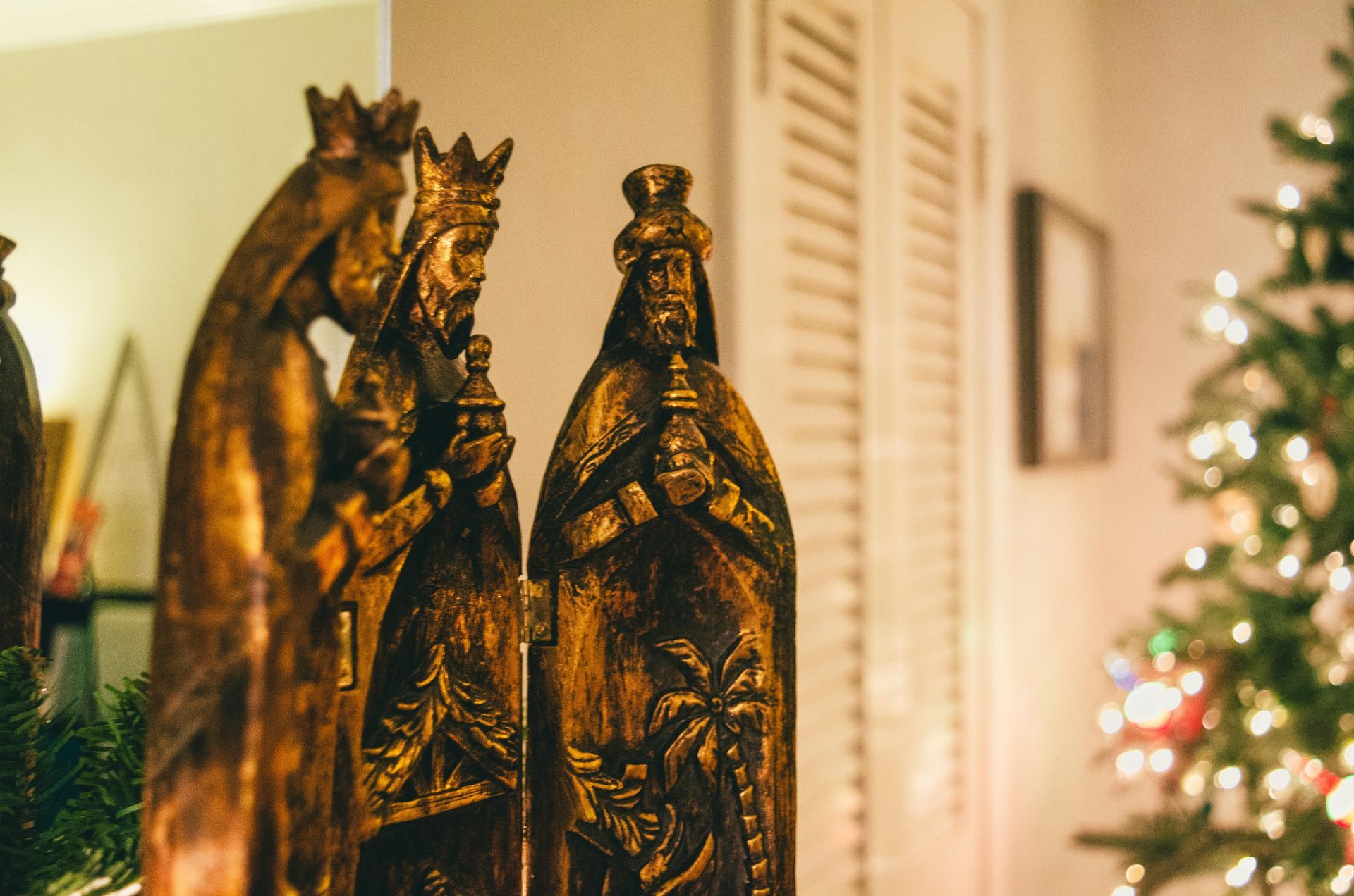 Three wooden wise men statues with a Christmas tree in the background.