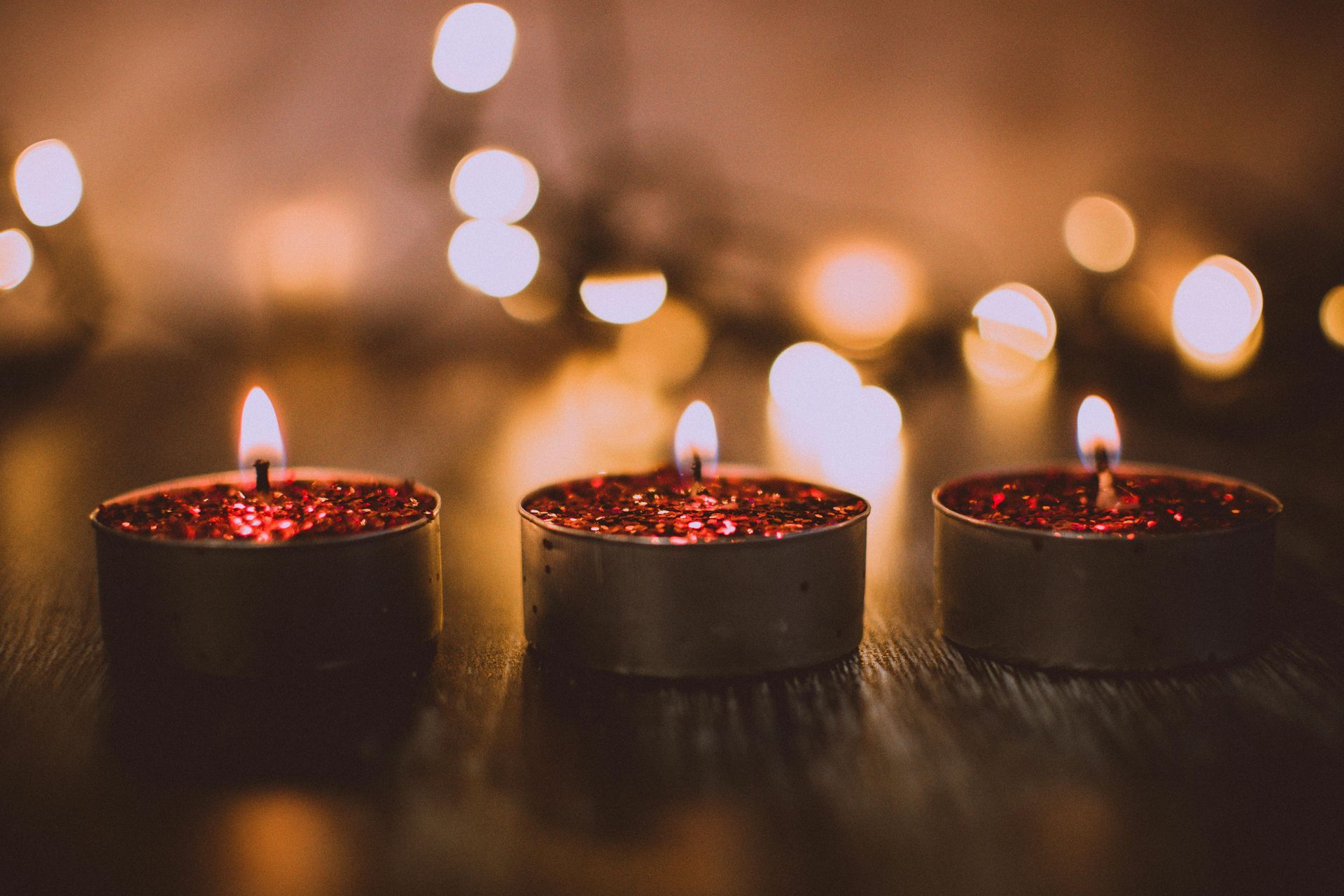 Three lit candles with sparkling red glitter and blurry lights in the background.
