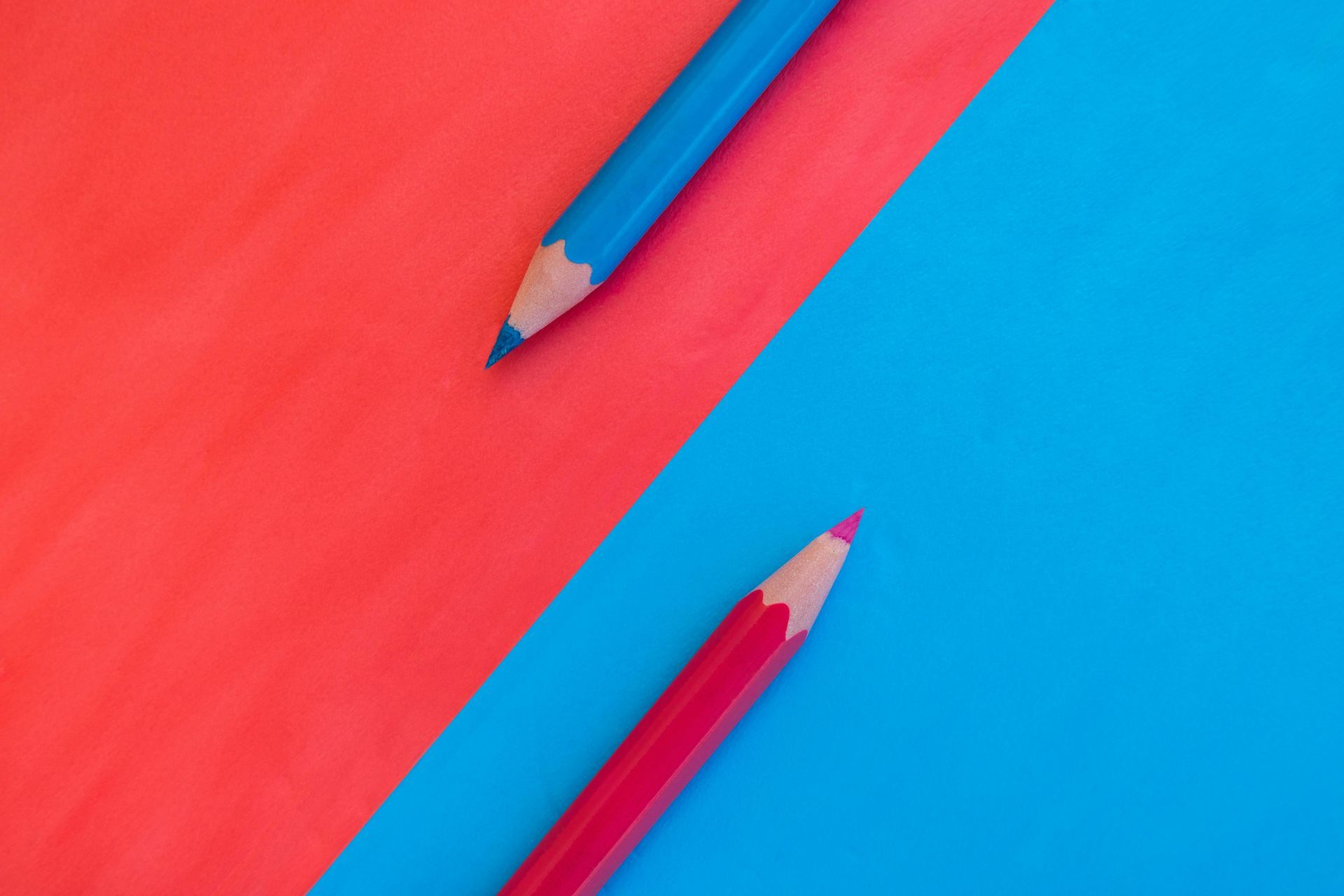 Two sharpened pencils crossing on a red and blue background