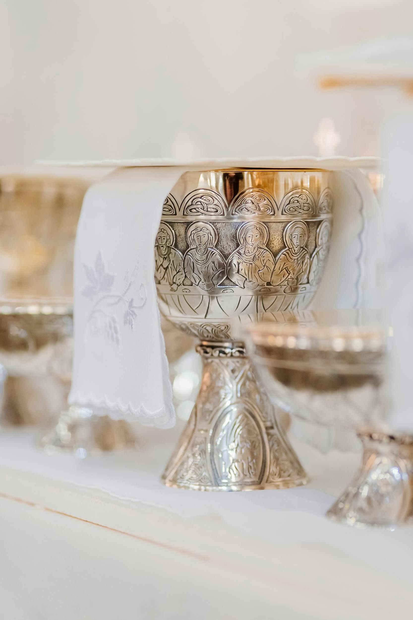 Silver chalice with ornate details, draped with a white linen cloth, on a table.