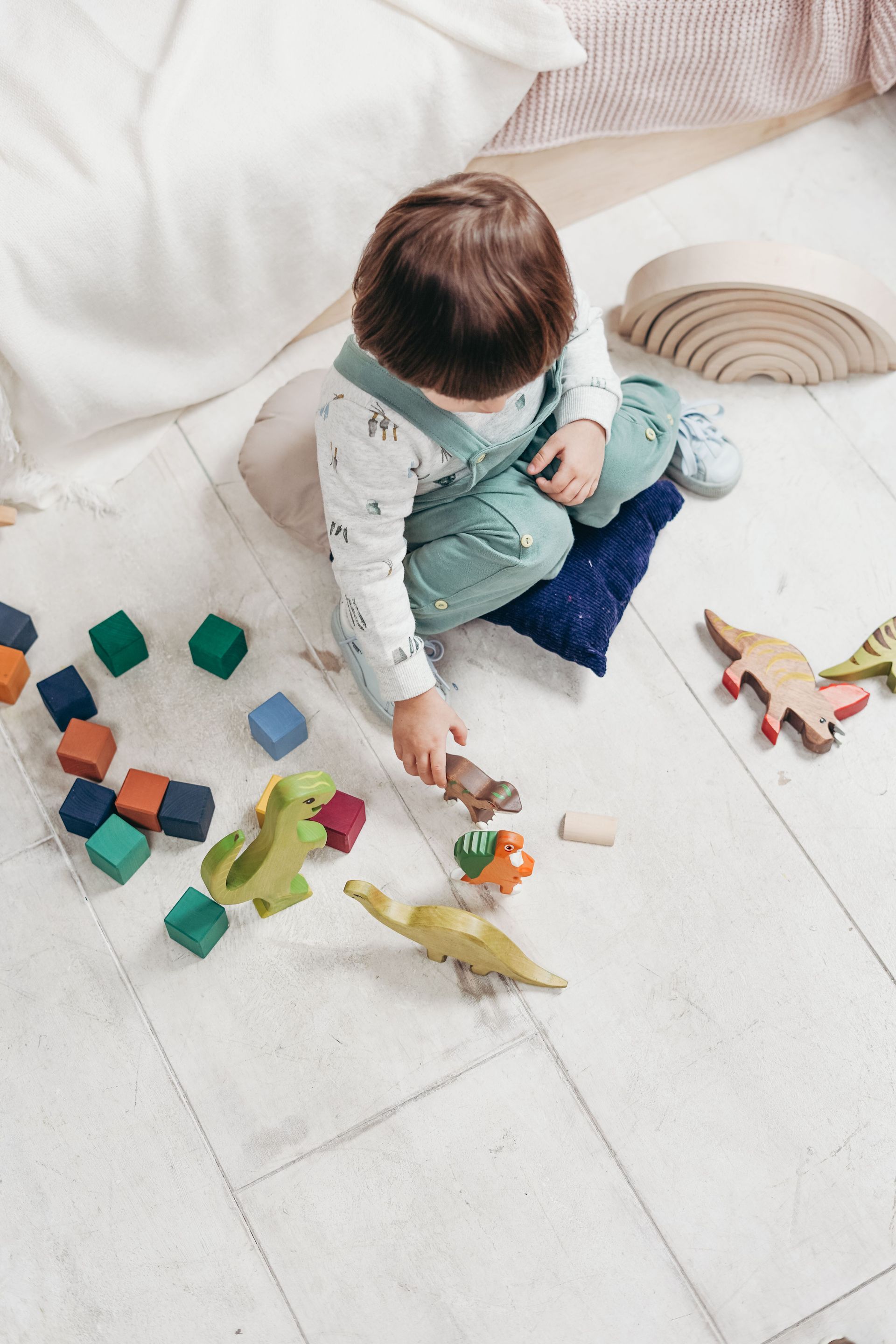 Child playing with colorful blocks and toy animals on a white floor near a sofa
