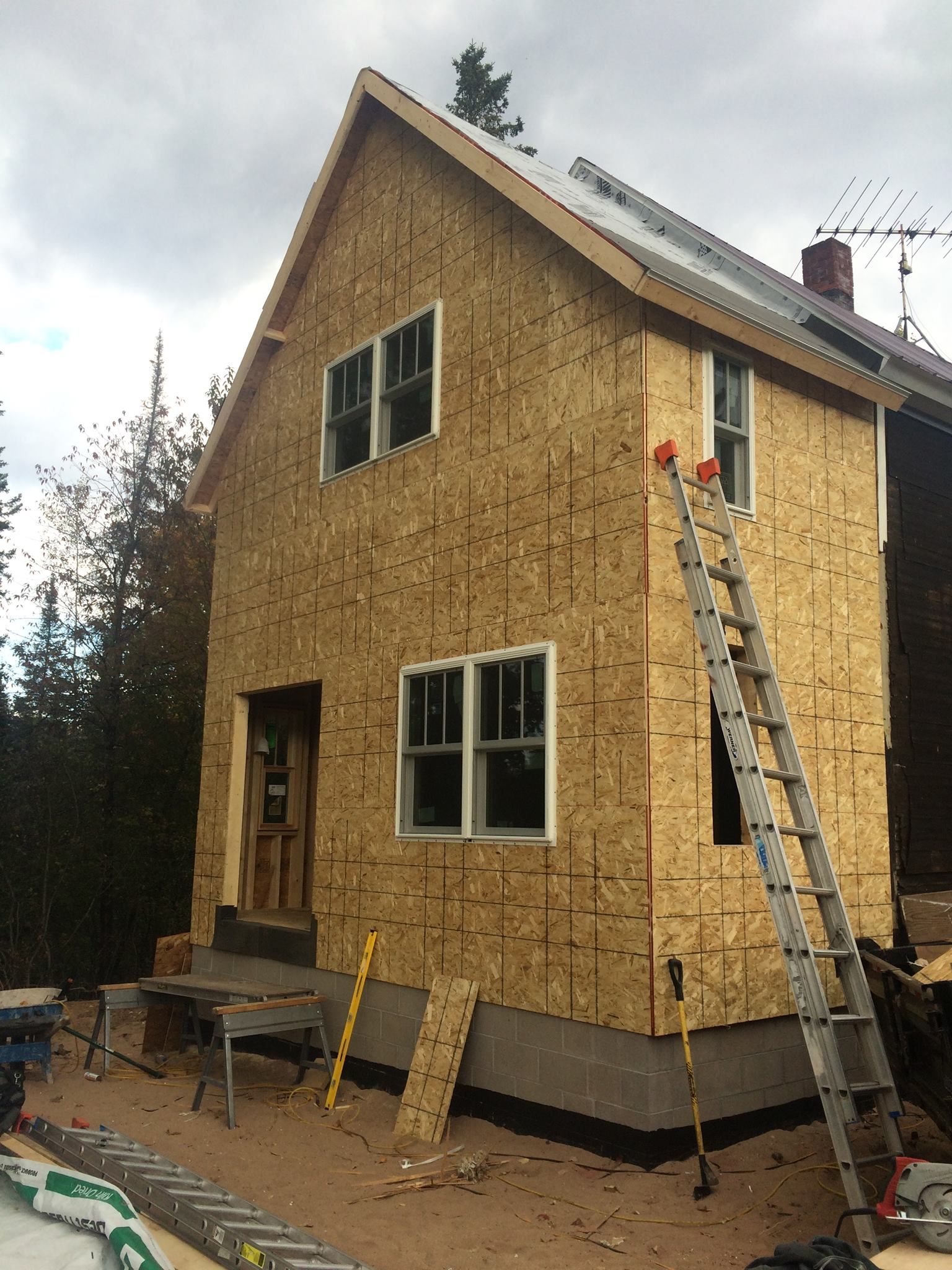 House under construction with exposed plywood siding, ladders, and building materials outside.