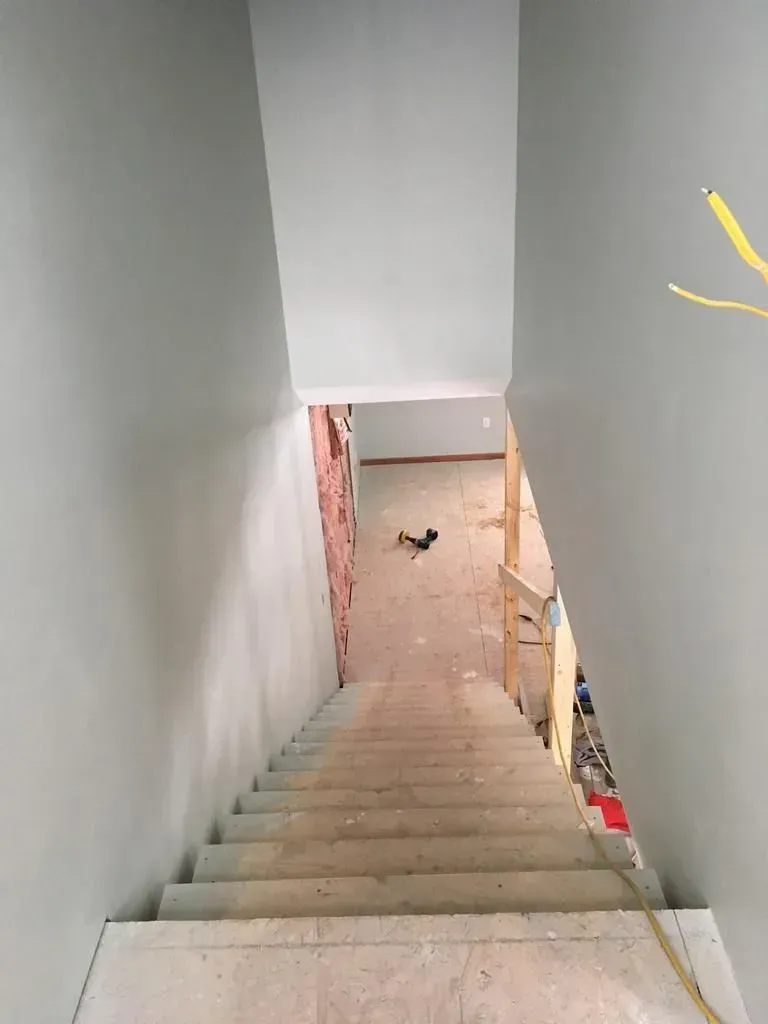 Stairwell descending to a lower floor with gray walls and unfinished construction materials below