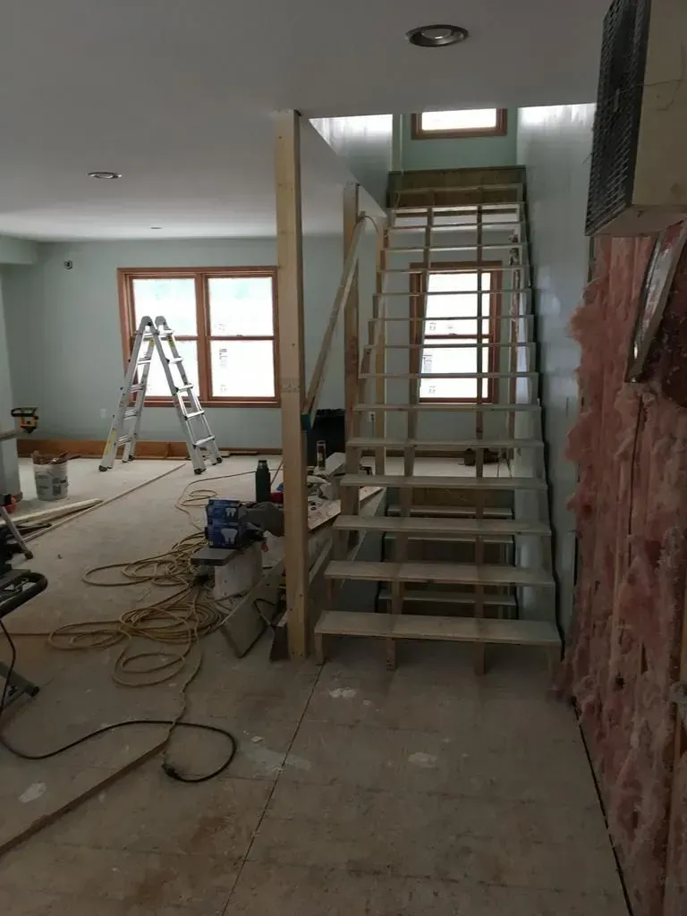 Renovation site with a central staircase, ladder, tools, and exposed wiring inside a partially finished room