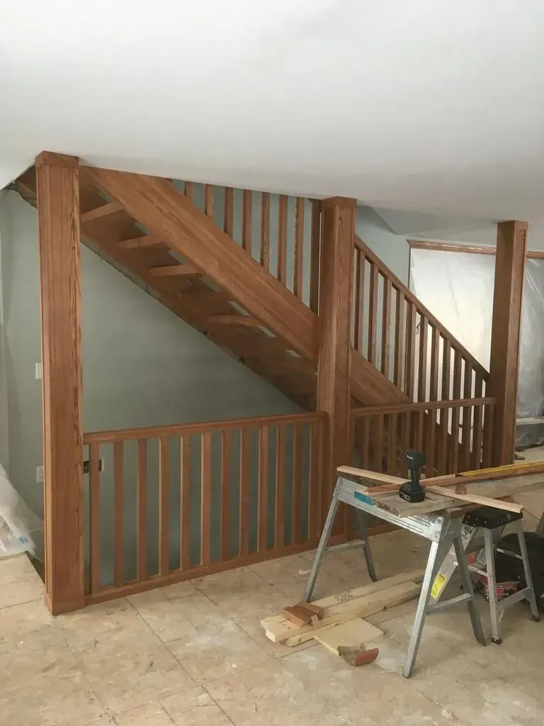 Wooden staircase with railing in a home interior, with a workbench in the foreground.