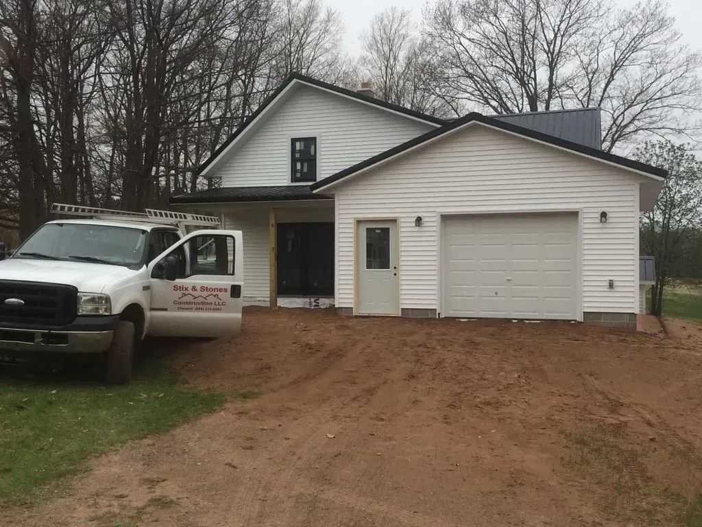 White house with attached garage and a white pickup truck parked in front on a muddy driveway.