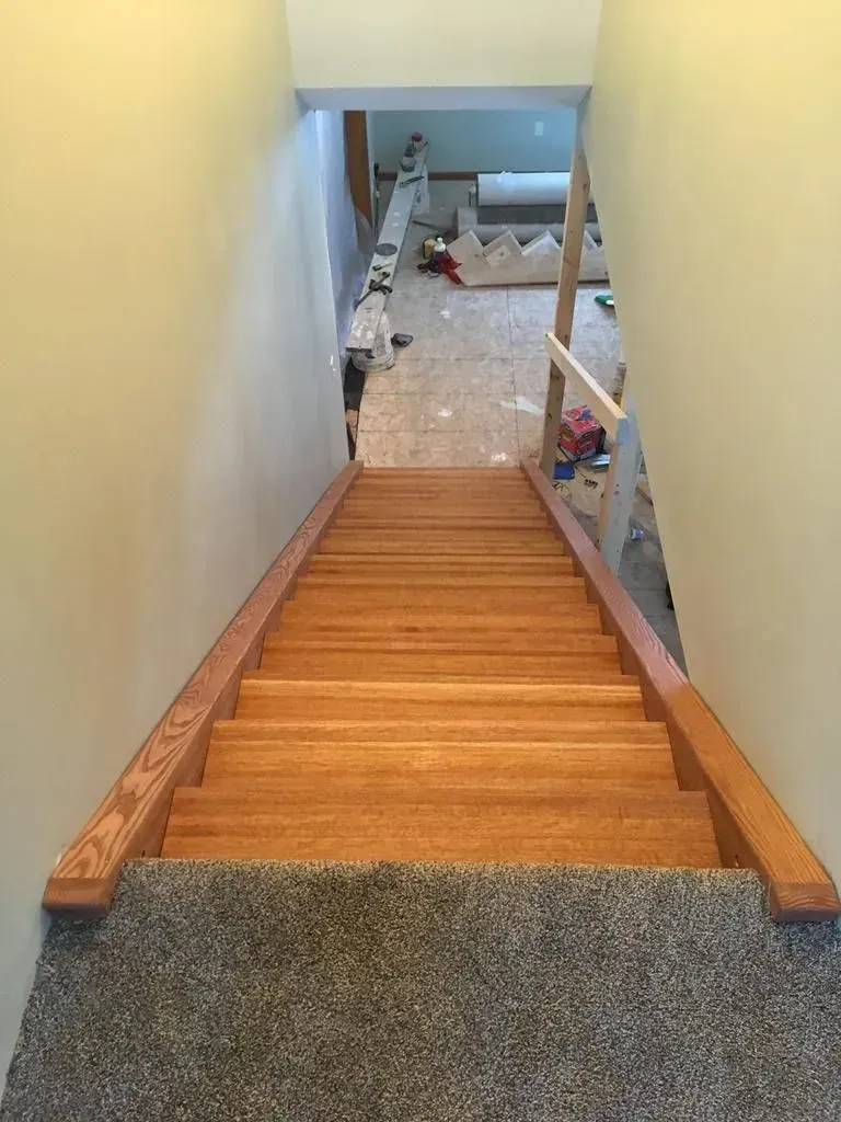 Wooden staircase with carpeted steps leading down to a cluttered room and renovation materials.
