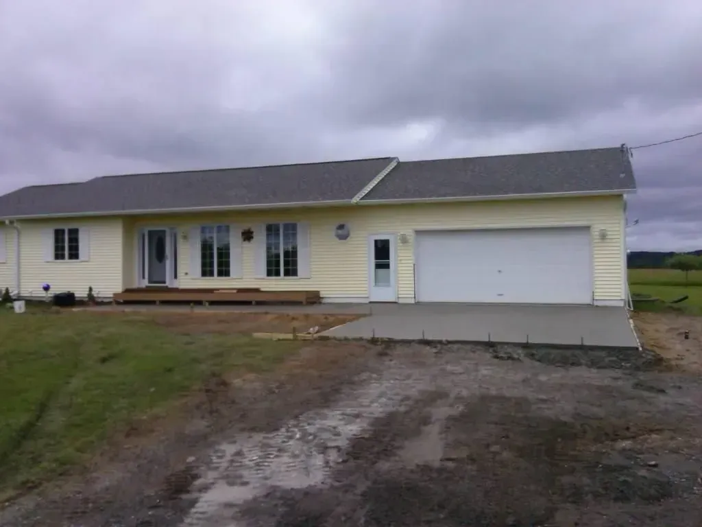 Single-story yellow house with attached garage and muddy driveway under cloudy skies