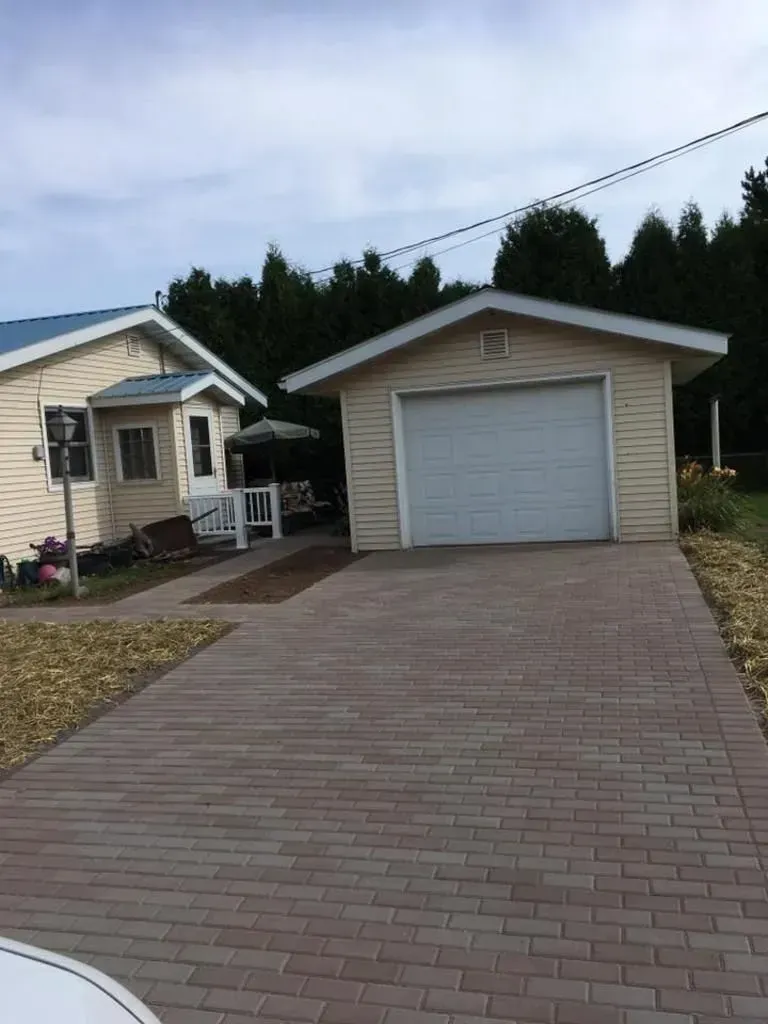 Driveway leading to a beige garage beside a house under a cloudy sky