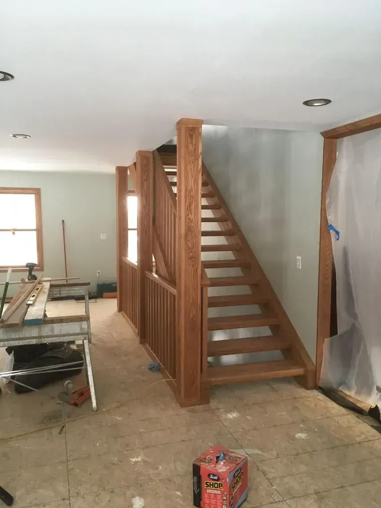 Unfinished interior with a wooden staircase, exposed floor, and construction materials in a room under renovation.