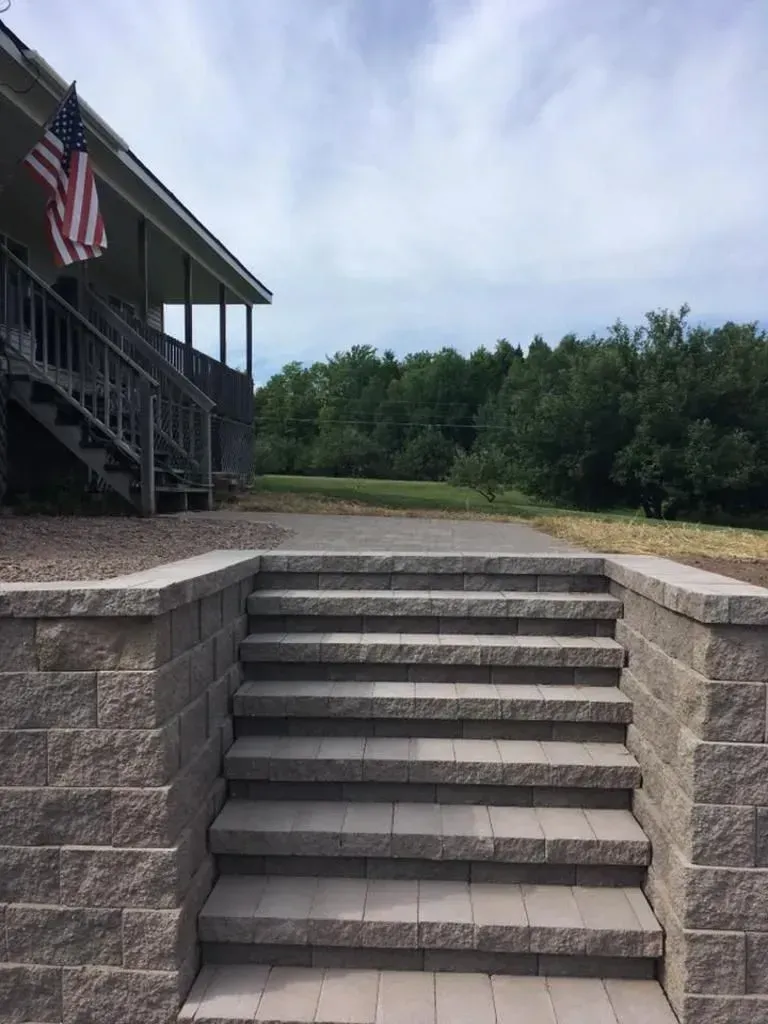 Stone steps leading to a porch with an American flag, beside a grassy yard and trees