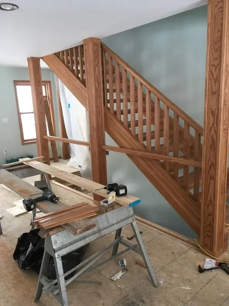 Wooden staircase railing under construction in a room with tools and lumber nearby