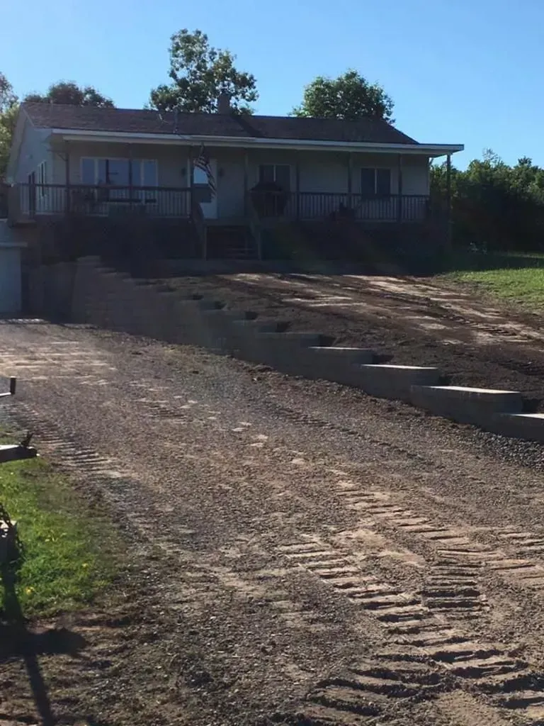 House at top of a steep gravel driveway, with steps and trees in bright sunlight