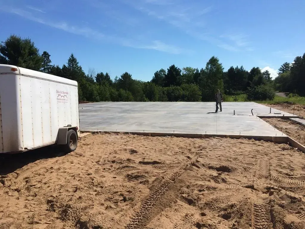 New concrete slab under construction with a white trailer on the left and a worker in the distance