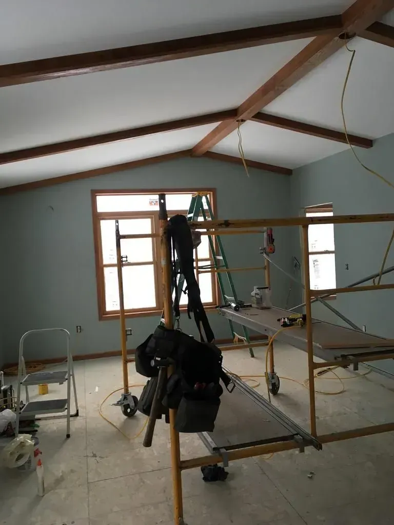 Scaffolding in a room with white walls, exposed wood beams, and windows during renovation.