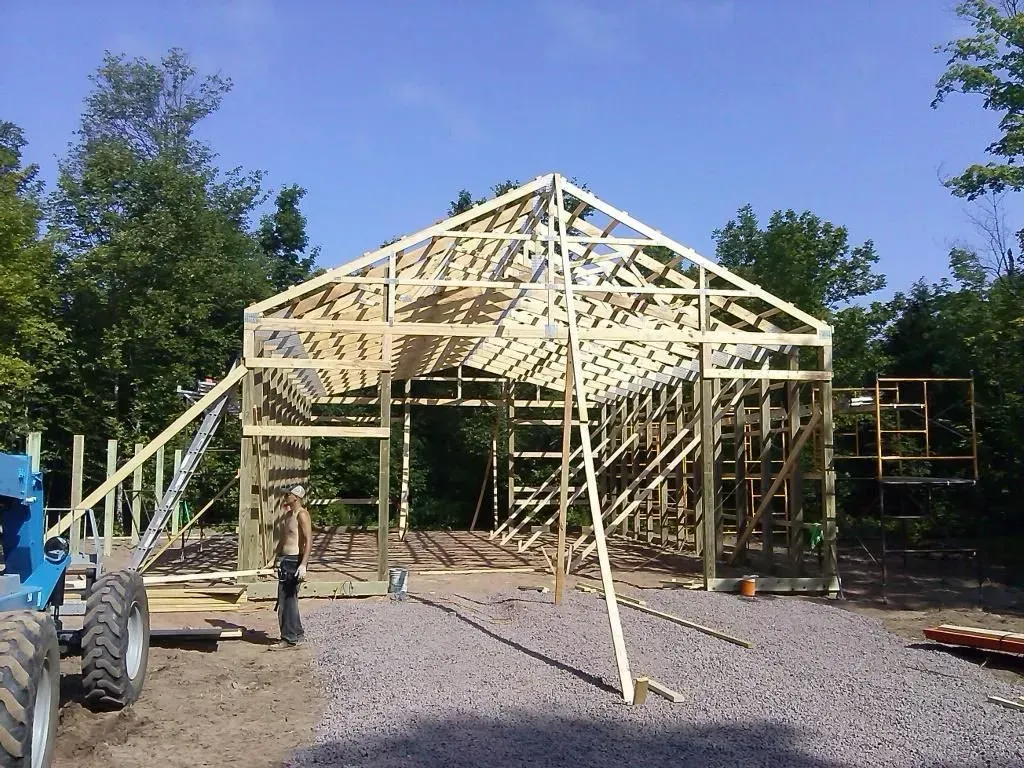 Wooden frame of a house under construction with workers, blue sky, and trees in the background
