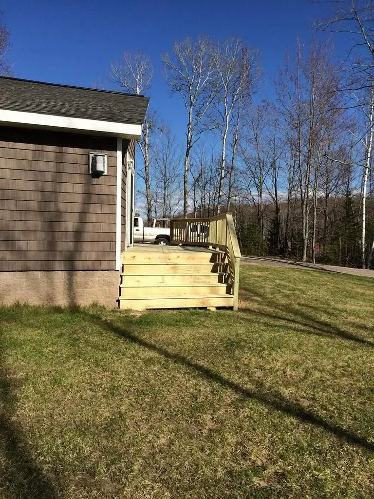 Wooden steps beside a house lead down to a grassy yard under a clear blue sky.