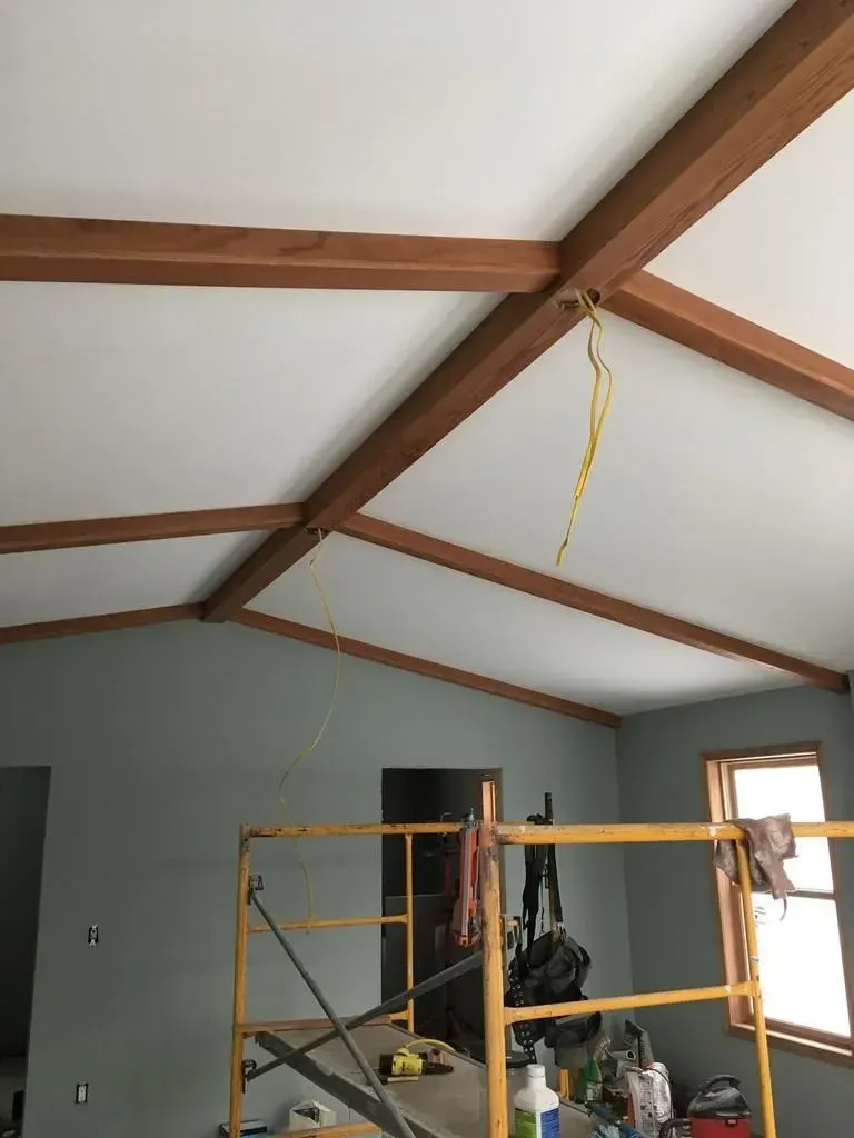 Room with vaulted ceiling, exposed wood beams, and a yellow scaffold in the center of the space.