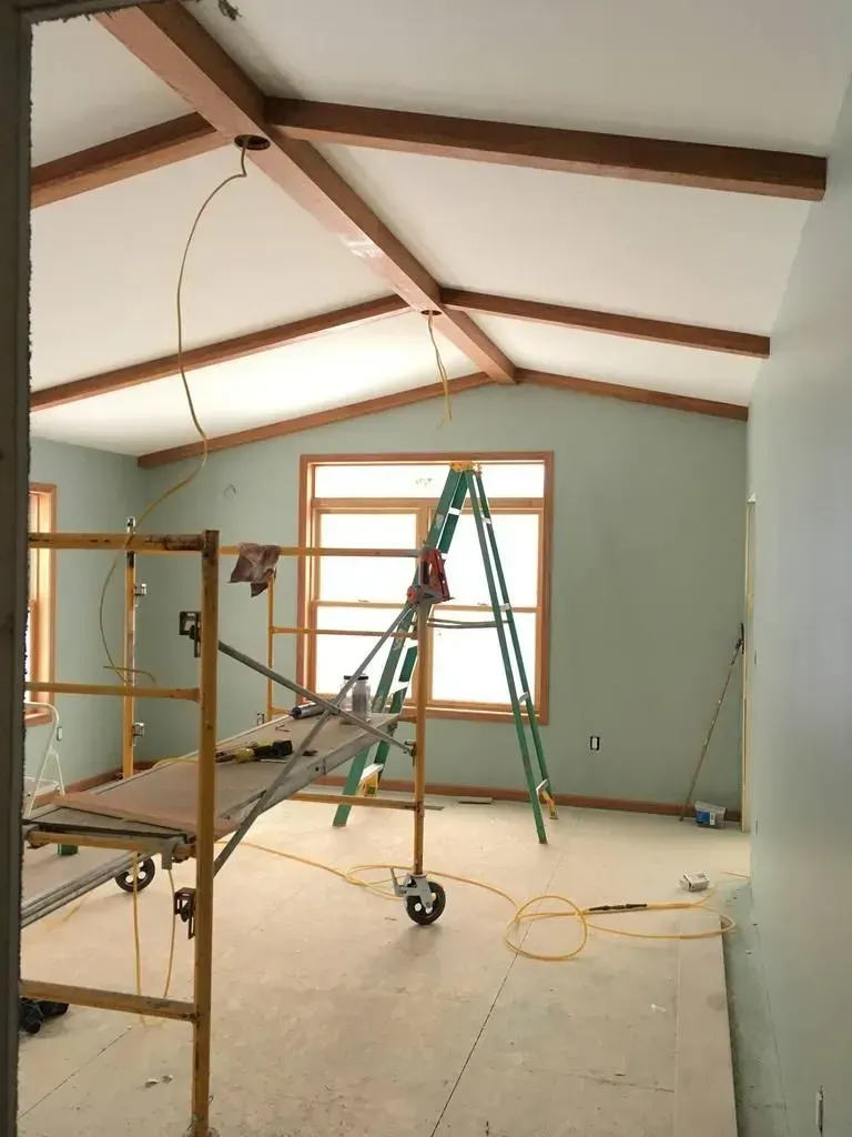 Interior room under renovation with ladders, scaffolding, and exposed vaulted ceiling beams