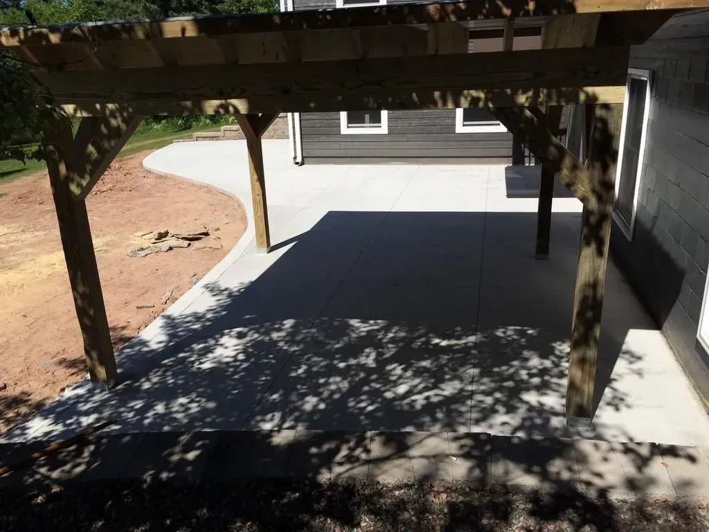 Shaded concrete patio under a wooden pergola beside a house