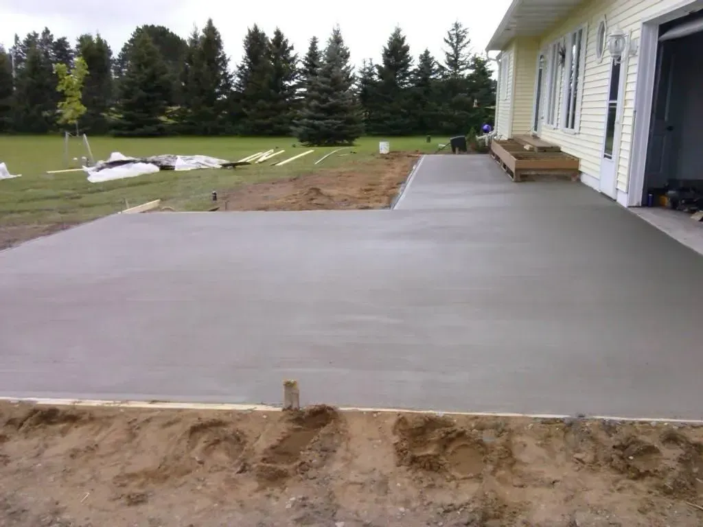 Concrete patio next to a house, with a grassy yard and trees in the background