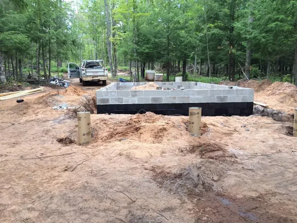 Raised foundation blocks in a wooded construction site with an excavator in the background