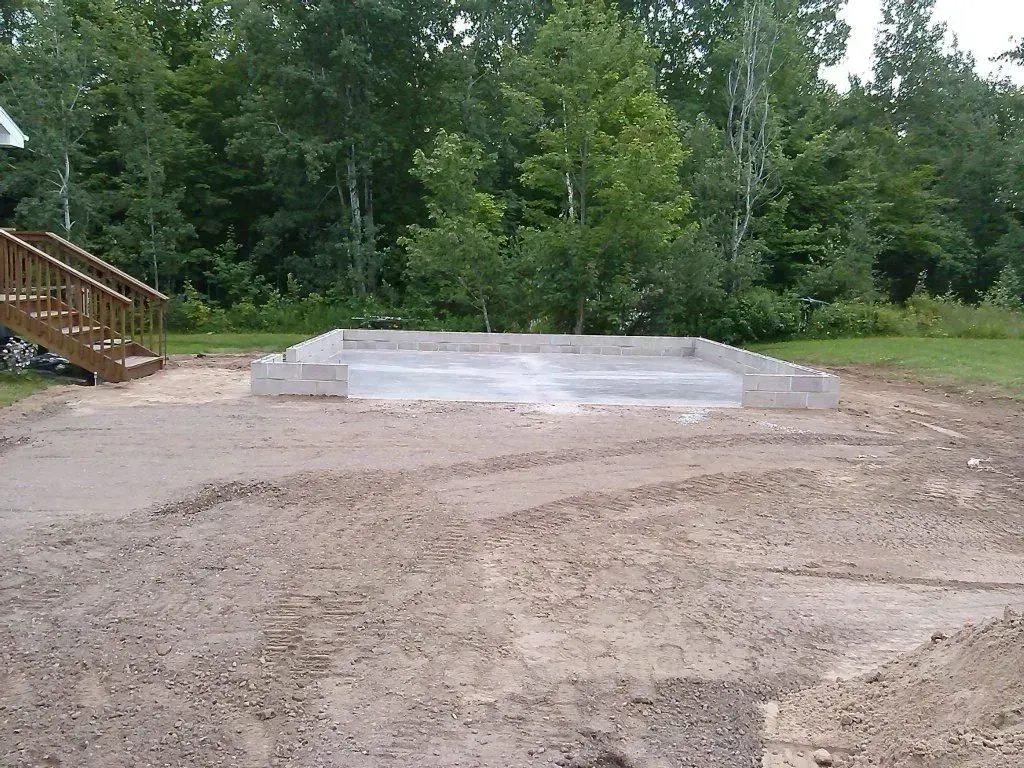 Concrete pad in a dirt clearing beside trees and a wooden staircase.