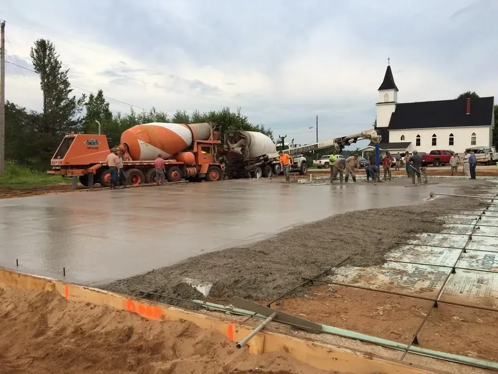 Orange cement mixer truck at a wet construction site with workers near a white building