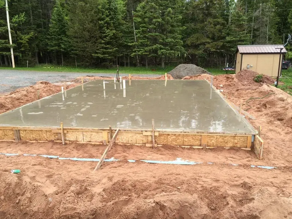Fresh concrete foundation slab at a wooded construction site, with stakes and forms around the edges.