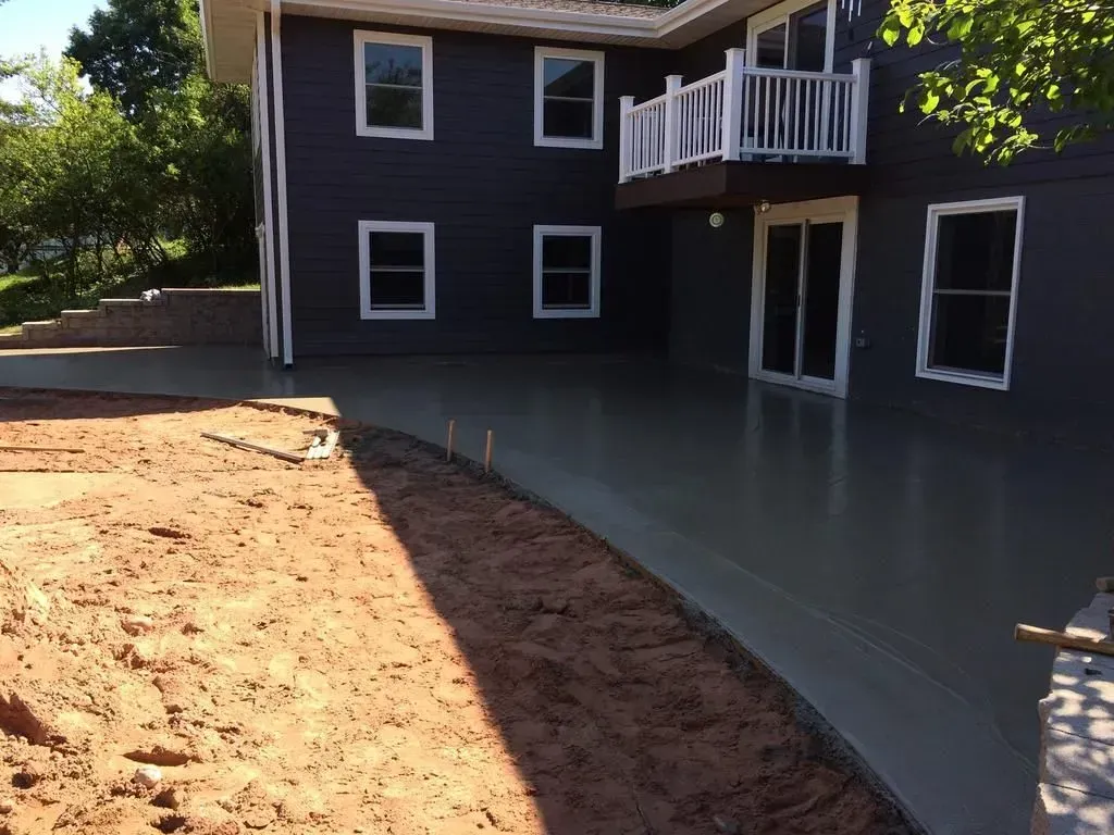 Freshly paved patio beside a dark house with white-trimmed windows and a small balcony