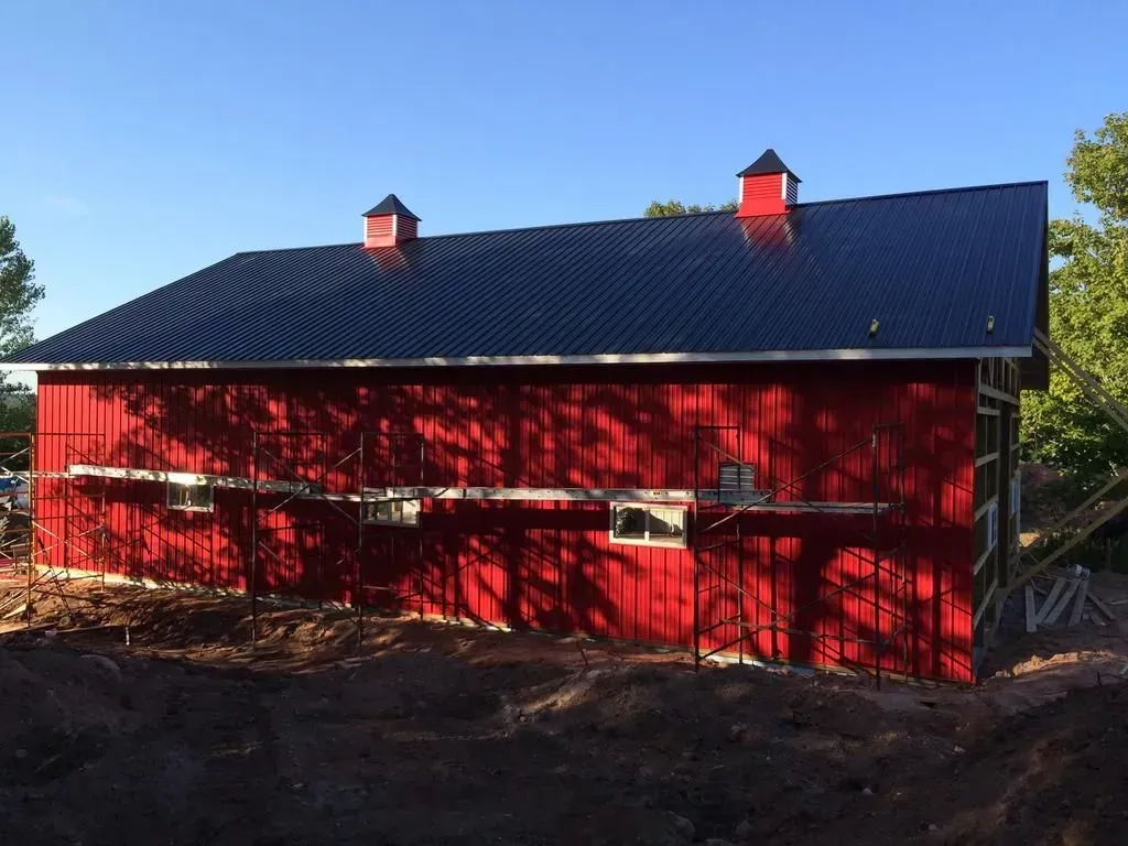 Red barn with a dark roof and two chimneys in a sunny rural setting
