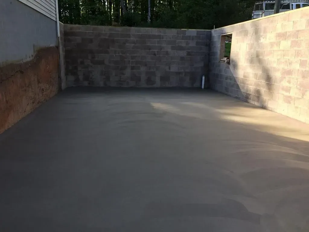 Empty concrete driveway enclosed by stone walls, with a small open area and trees above the back wall