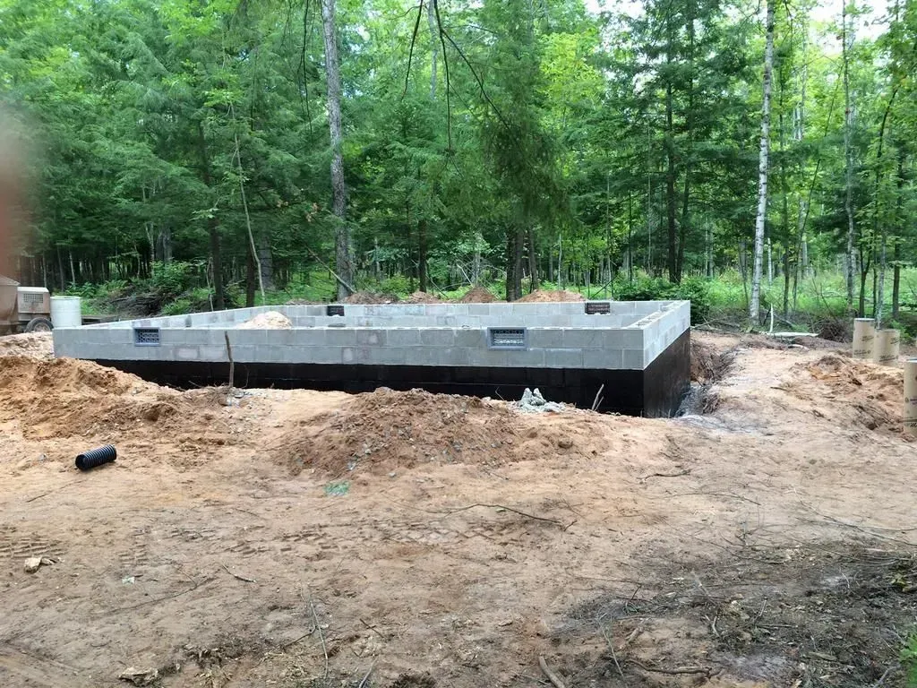 Concrete foundation site in a wooded area, with dirt excavated around a low rectangular slab.