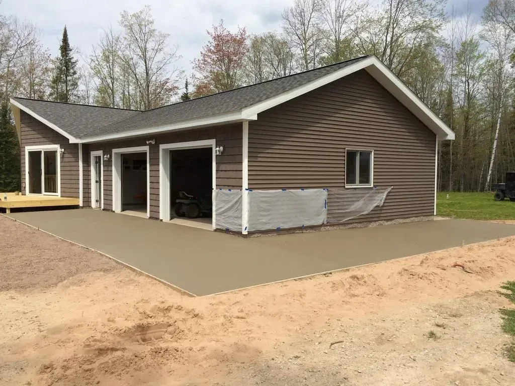 Brown house with attached garage and fresh concrete driveway in a wooded yard