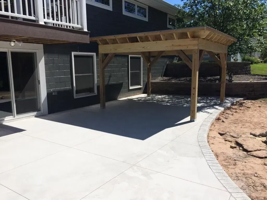 Backyard patio with a wooden pergola beside a dark house and curved stone border