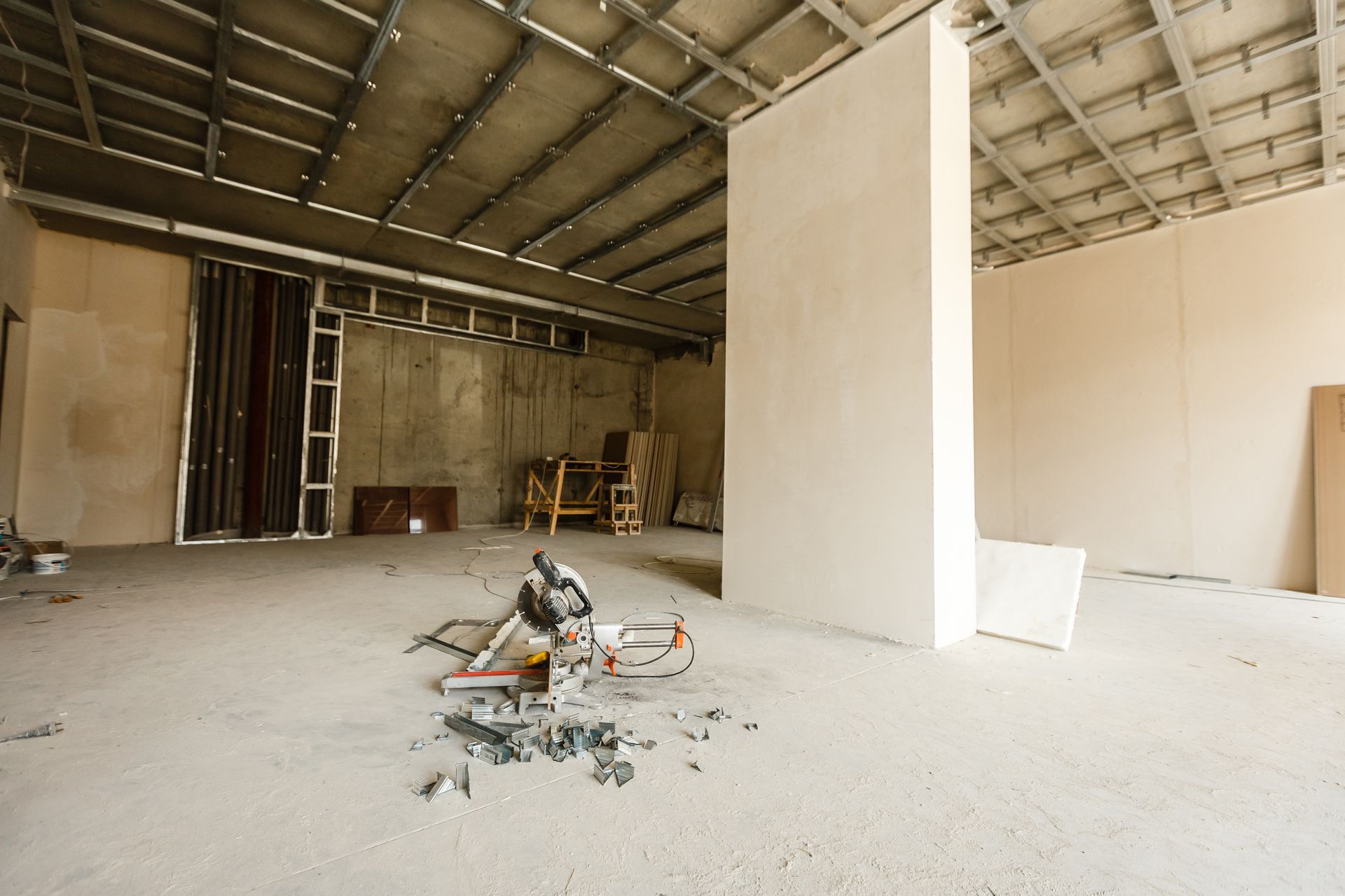Empty unfinished interior with exposed ceiling, drywall partitions, and construction tools on the floor