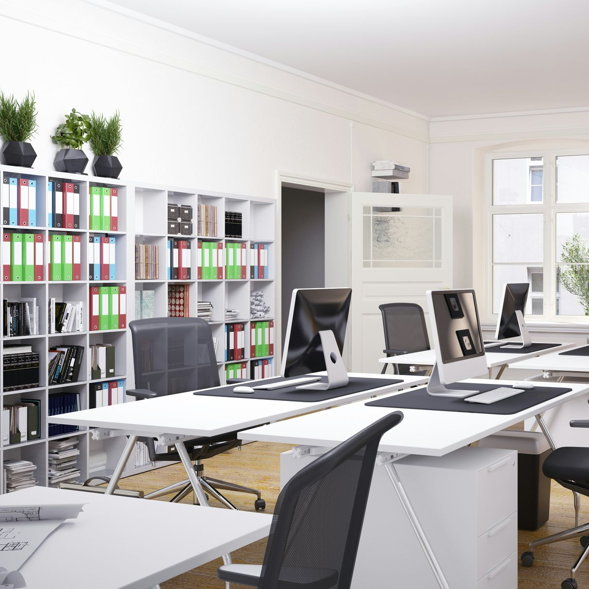Bright office interior with white desks, chairs, storage, and computers. Filing cabinets with colorful folders.
