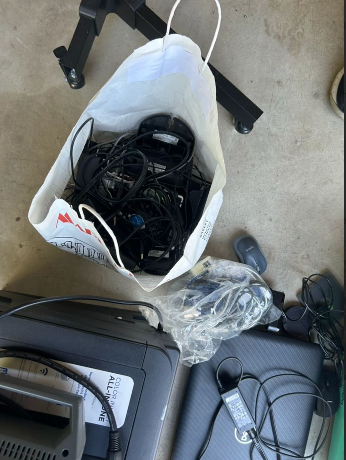 Bag of tangled black cords and electronics, next to a printer and other items.
