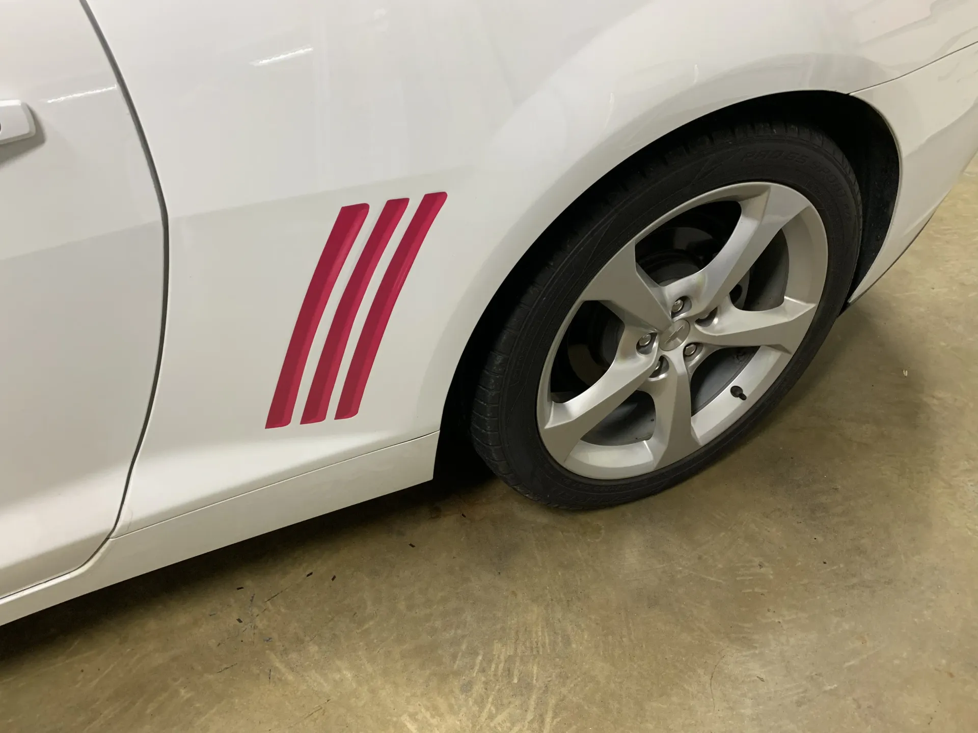 White car with three red stripes behind the front wheel.