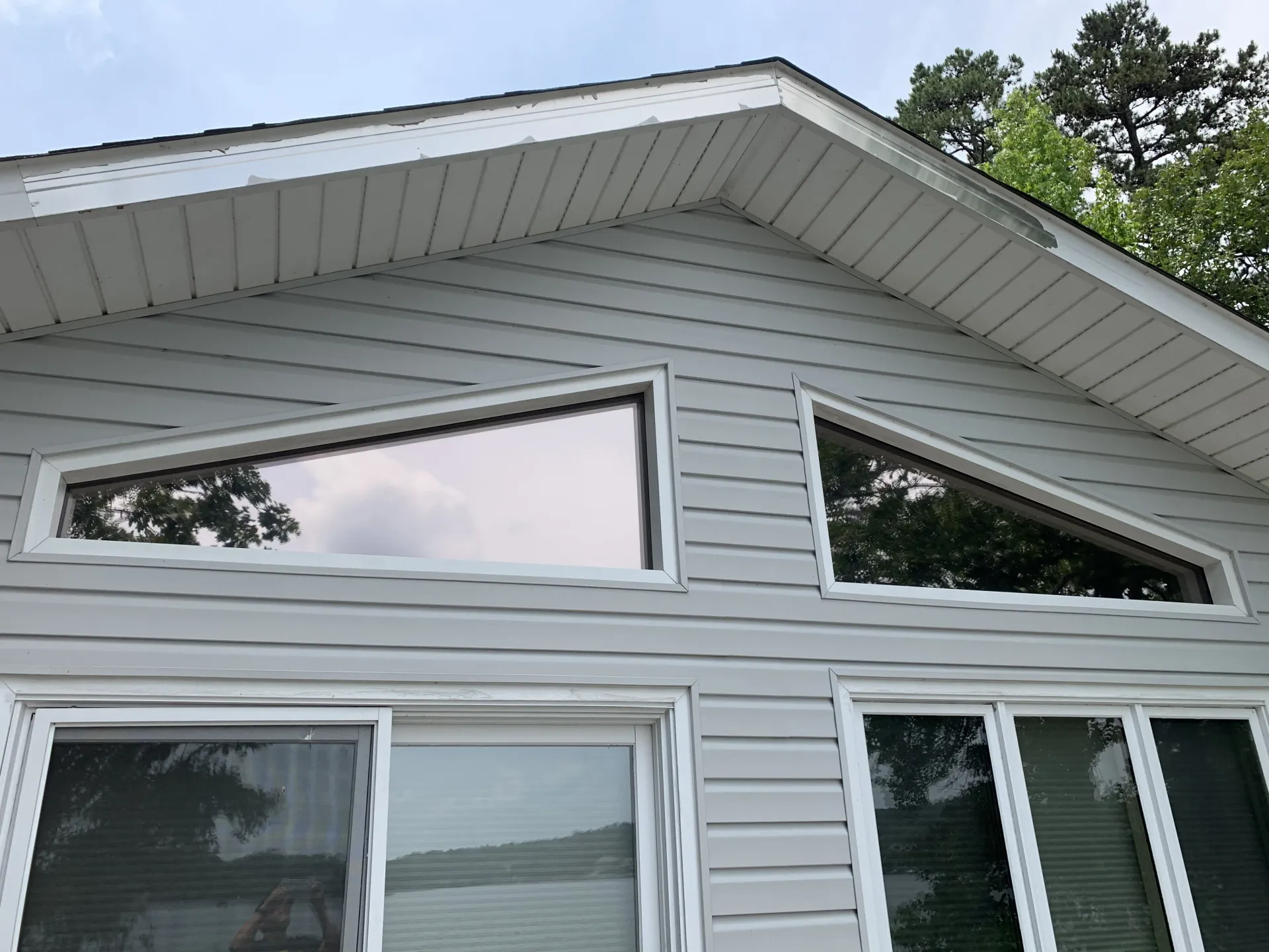 Gray house exterior with triangular windows under a peaked roof, and sliding glass doors below.