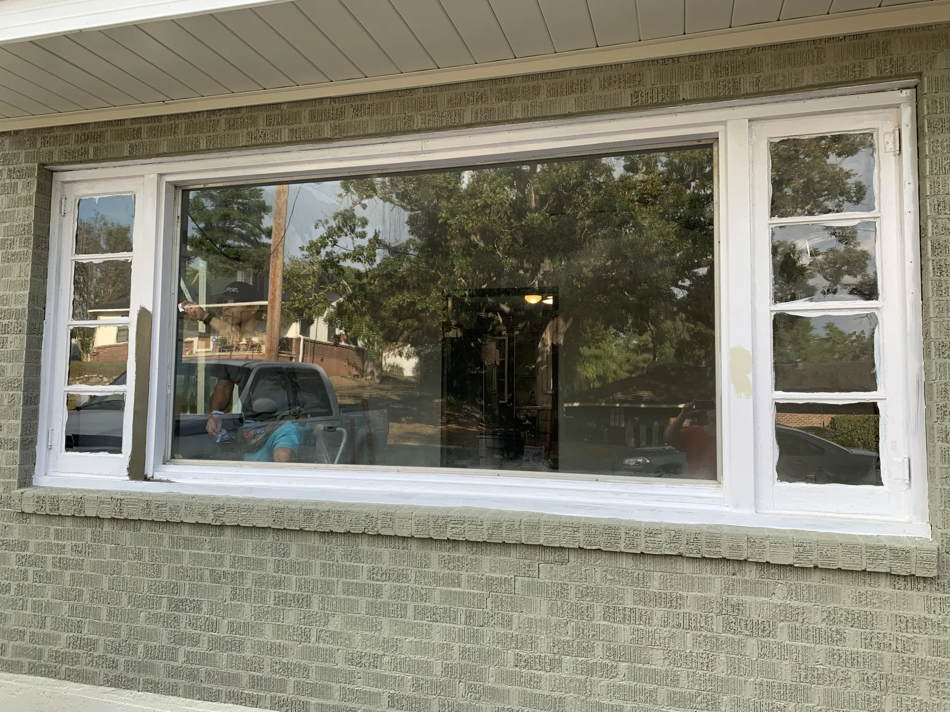 White-framed window on a textured, gray wall reflecting trees, a vehicle, and a building under a white overhang.