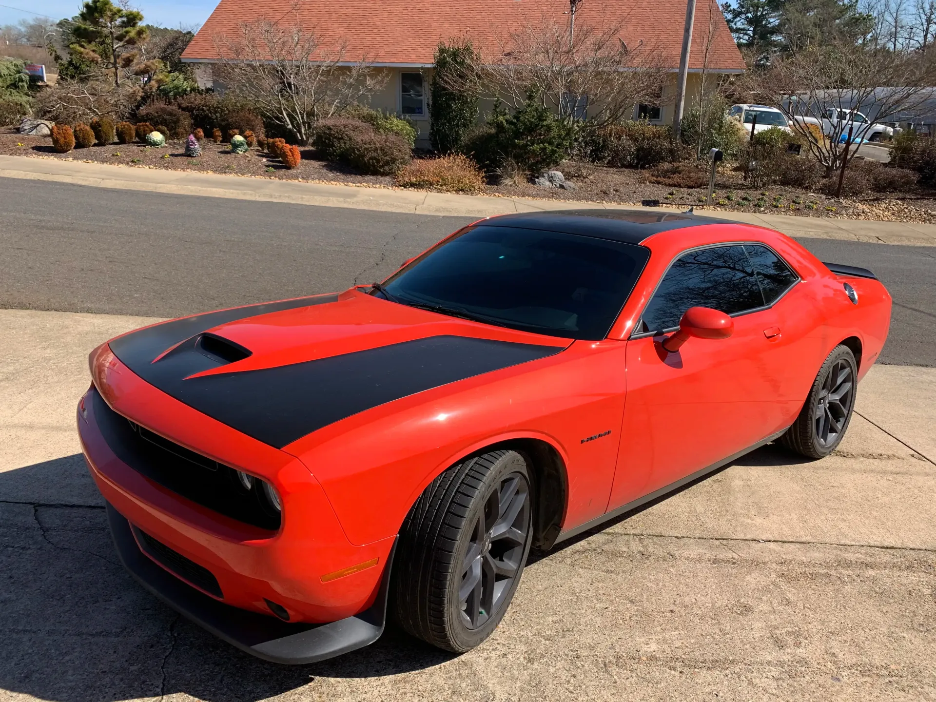 Red Dodge Challenger with black hood and roof parked on a paved driveway in front of a house.